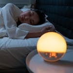 Woman sleeping peacefully in a cozy bedroom with ambient bedside light.